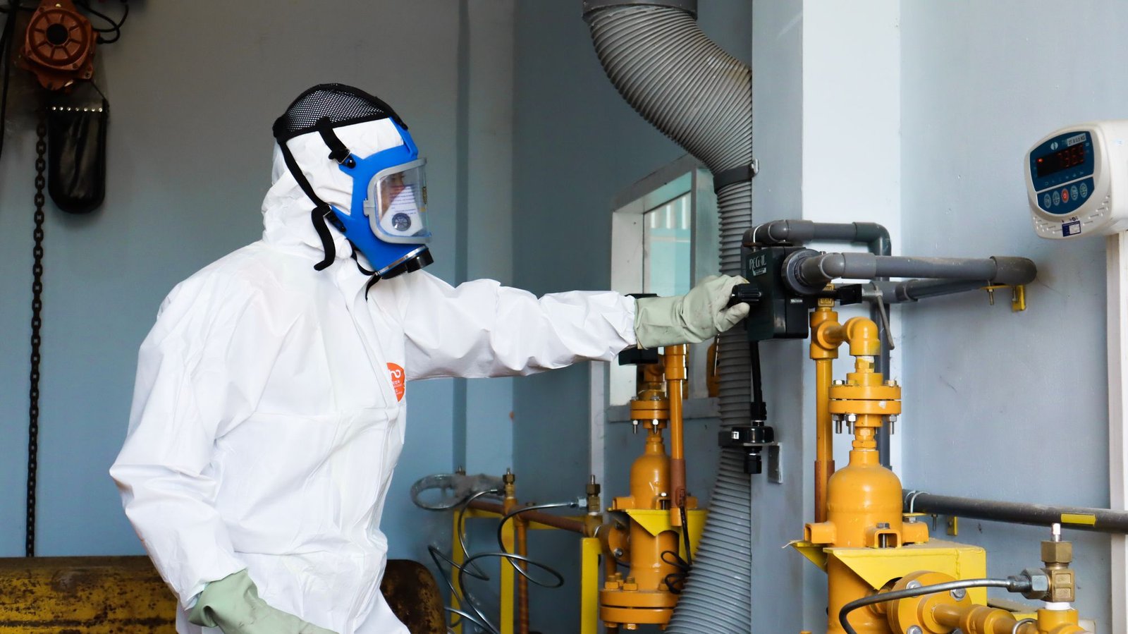 Trabalhador com traje e máscara de proteção completos operando equipamento em ambiente industrial